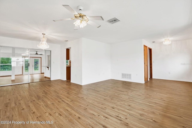 unfurnished living room featuring ceiling fan with notable chandelier, wood-type flooring, and french doors