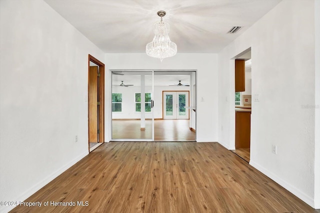 unfurnished dining area featuring a chandelier, wood-type flooring, and french doors