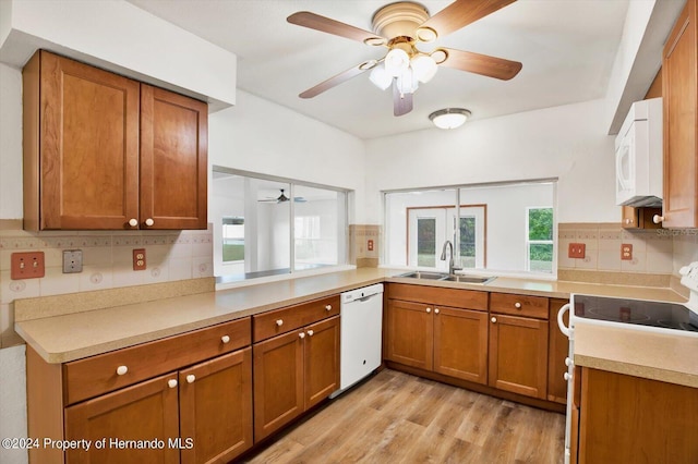 kitchen with sink, kitchen peninsula, white appliances, decorative backsplash, and light wood-type flooring