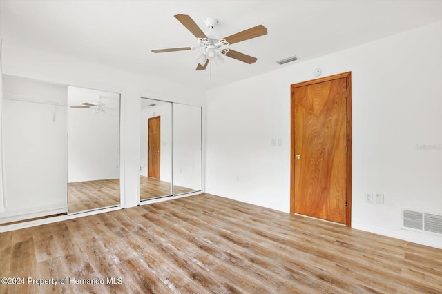 unfurnished bedroom featuring ceiling fan, light hardwood / wood-style flooring, and two closets