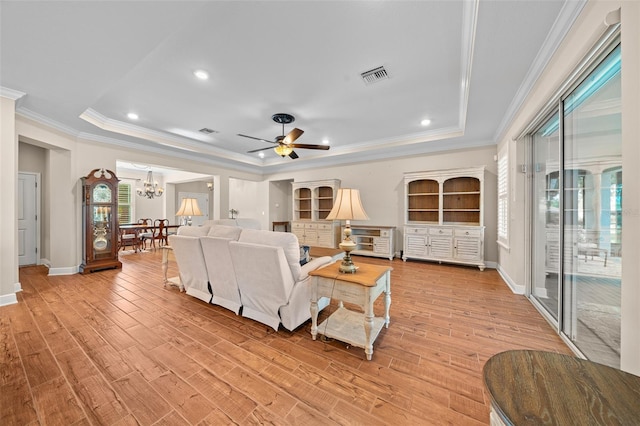 living room with ceiling fan with notable chandelier, a tray ceiling, light hardwood / wood-style flooring, and ornamental molding