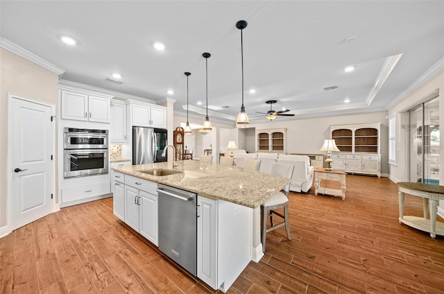 kitchen featuring stainless steel appliances, ceiling fan, sink, white cabinetry, and an island with sink