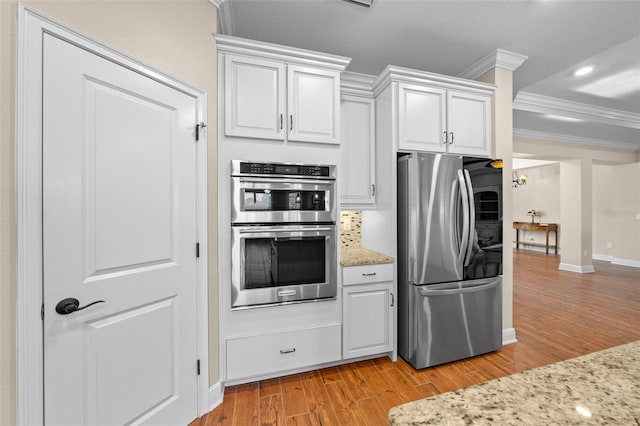 kitchen with white cabinets, ornamental molding, light hardwood / wood-style floors, light stone counters, and stainless steel appliances