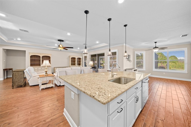 kitchen with pendant lighting, a kitchen island with sink, sink, light stone counters, and white cabinetry