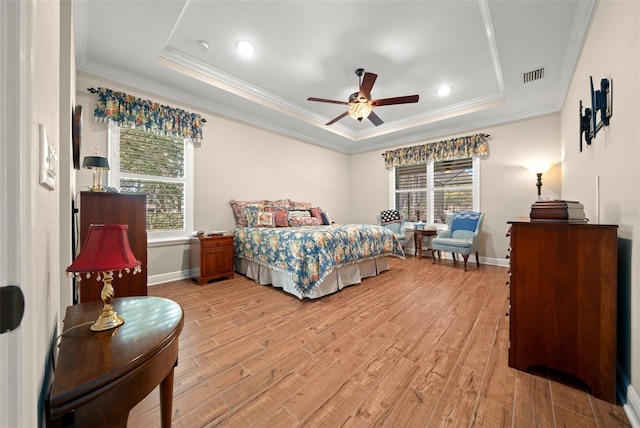 bedroom featuring light wood-type flooring, ornamental molding, a tray ceiling, ceiling fan, and multiple windows