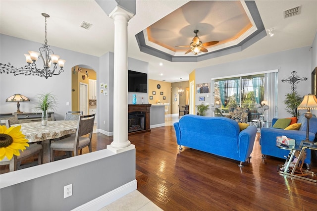 living room with ceiling fan with notable chandelier, dark hardwood / wood-style flooring, and a tray ceiling