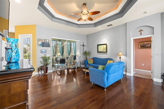 living room with dark hardwood / wood-style floors, a raised ceiling, ceiling fan, and crown molding