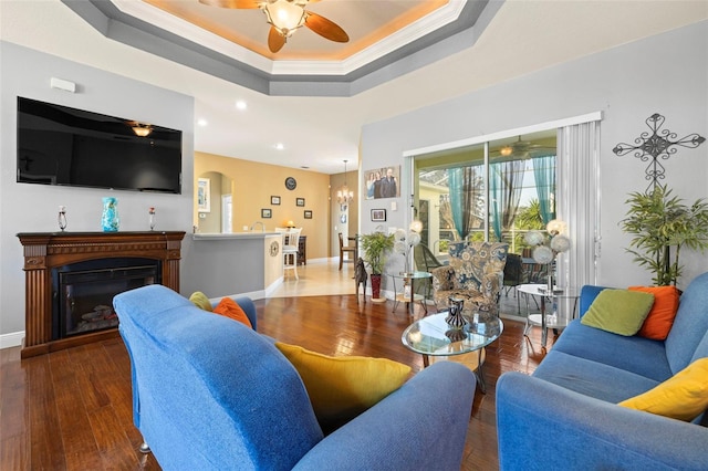 living room with dark hardwood / wood-style floors, a raised ceiling, ceiling fan, and crown molding