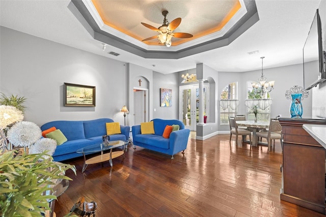 living room featuring a textured ceiling, ceiling fan with notable chandelier, a raised ceiling, dark wood-type flooring, and crown molding