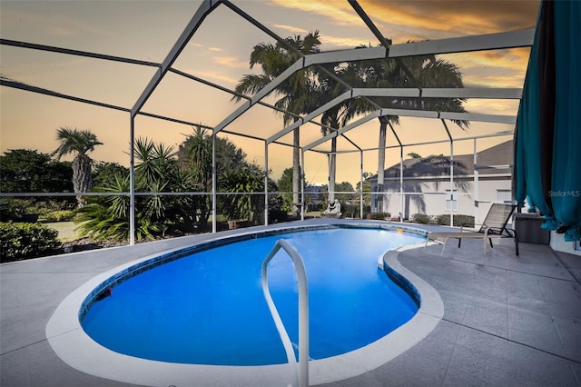 pool at dusk with glass enclosure and a patio area