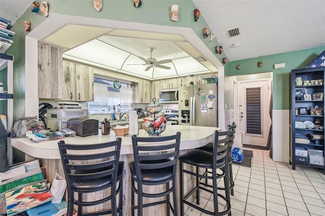 kitchen featuring light brown cabinets, ceiling fan, a textured ceiling, light tile patterned flooring, and stainless steel appliances