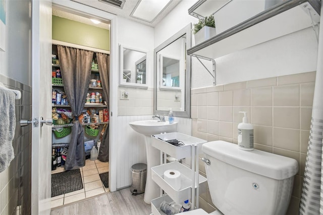 bathroom with toilet, wood-type flooring, and tile walls