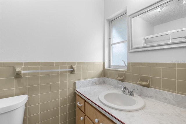 bathroom with a textured ceiling, vanity, toilet, and tile walls