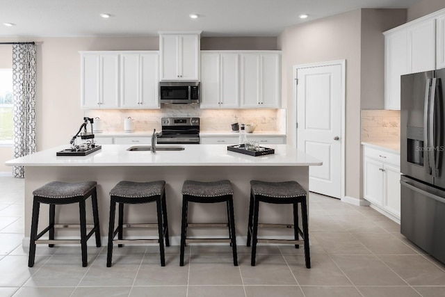 kitchen featuring a kitchen bar, a kitchen island with sink, white cabinets, and appliances with stainless steel finishes