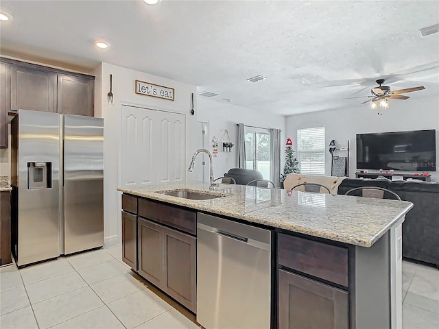 kitchen featuring light stone counters, stainless steel appliances, ceiling fan, a kitchen island with sink, and sink