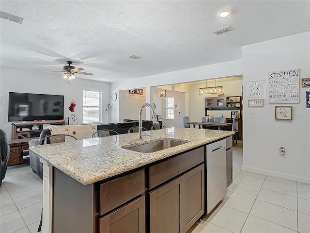 kitchen with a center island with sink, dishwasher, light stone counters, and sink