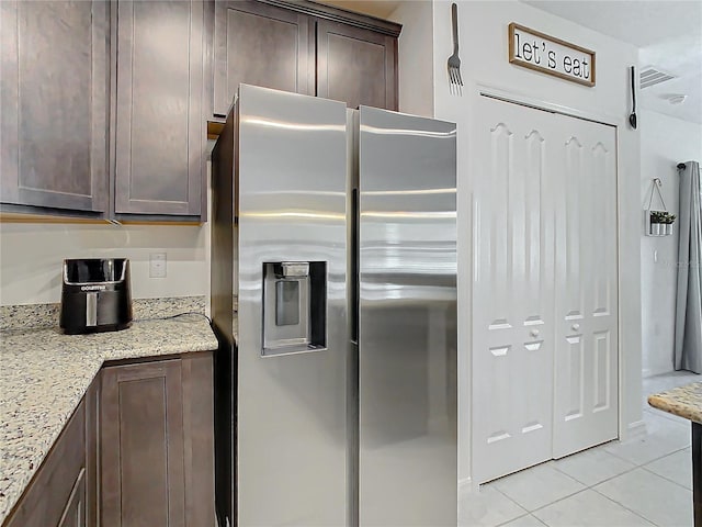 kitchen with light stone countertops, stainless steel fridge with ice dispenser, dark brown cabinetry, and light tile patterned flooring