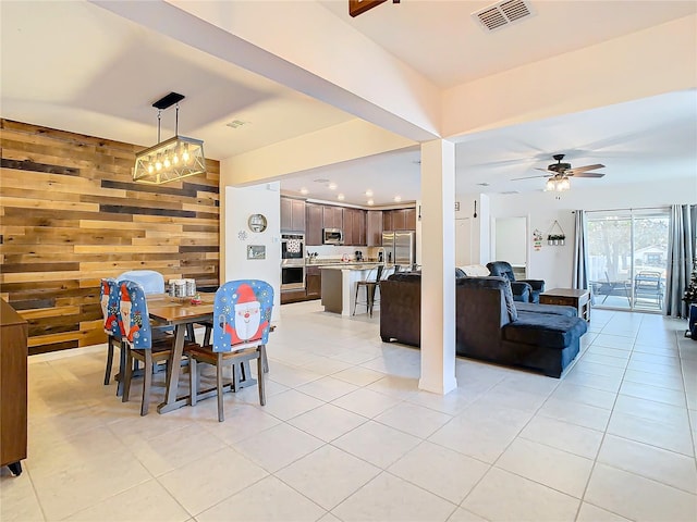 dining space with ceiling fan, wooden walls, and light tile patterned flooring