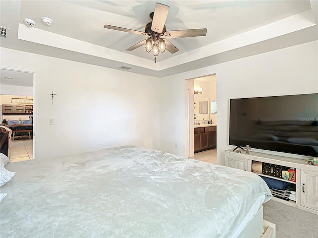 bedroom featuring ceiling fan, a raised ceiling, light colored carpet, and ensuite bath