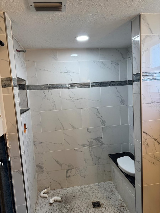 bathroom with a tile shower and a textured ceiling