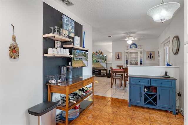 interior space featuring blue cabinets, ceiling fan, light tile patterned floors, a textured ceiling, and decorative light fixtures