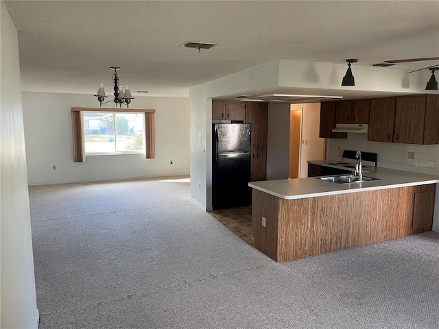 kitchen featuring black refrigerator, light carpet, kitchen peninsula, sink, and an inviting chandelier