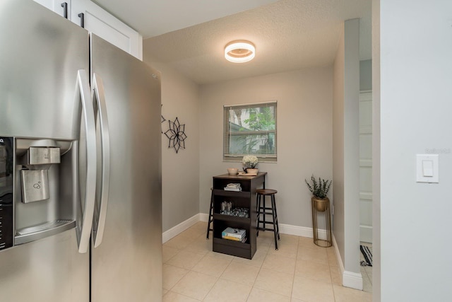 kitchen with white cabinets, stainless steel fridge, light tile patterned flooring, and a textured ceiling