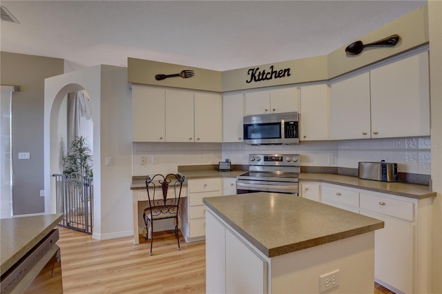 kitchen featuring decorative backsplash, appliances with stainless steel finishes, light wood-type flooring, white cabinets, and a kitchen island