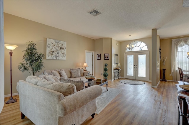 living room featuring french doors, light wood-type flooring, a textured ceiling, an inviting chandelier, and lofted ceiling