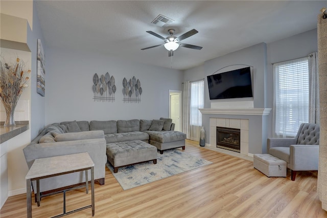 living room with light hardwood / wood-style flooring, ceiling fan, and a tiled fireplace