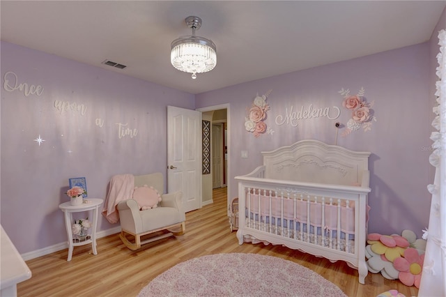 bedroom with a crib, light hardwood / wood-style floors, and a chandelier