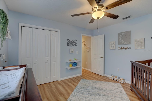 bedroom featuring a crib, a closet, light hardwood / wood-style floors, and ceiling fan