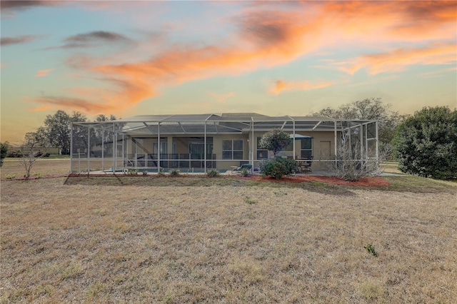 back house at dusk featuring a lawn and glass enclosure