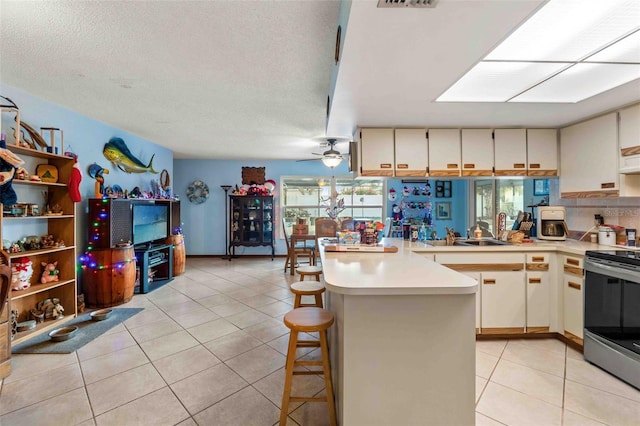 kitchen featuring a kitchen breakfast bar, kitchen peninsula, a textured ceiling, electric stove, and light tile patterned flooring