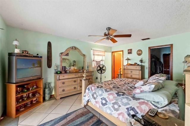 bedroom featuring a walk in closet, a textured ceiling, ceiling fan, light tile patterned floors, and a closet