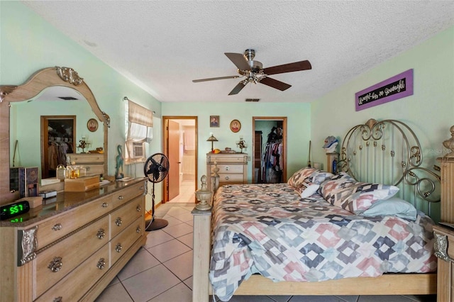 bedroom with a walk in closet, ceiling fan, a textured ceiling, light tile patterned flooring, and a closet