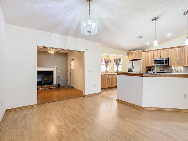 kitchen with decorative backsplash, light wood-type flooring, stainless steel appliances, hanging light fixtures, and lofted ceiling