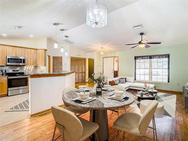 dining room with ceiling fan with notable chandelier, light wood-type flooring, lofted ceiling, and a textured ceiling