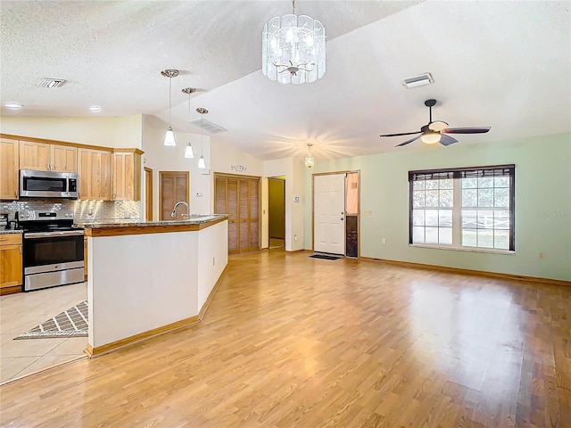 kitchen featuring stainless steel appliances, a textured ceiling, decorative light fixtures, vaulted ceiling, and light wood-type flooring