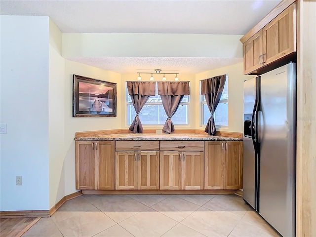 kitchen featuring a textured ceiling, light stone counters, light tile patterned floors, and stainless steel refrigerator with ice dispenser