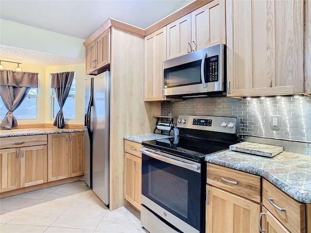 kitchen with appliances with stainless steel finishes, backsplash, light stone counters, light tile patterned floors, and light brown cabinets