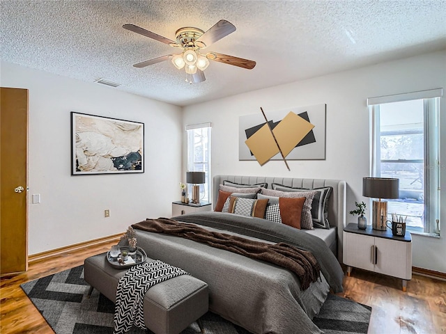 bedroom with wood-type flooring, a textured ceiling, multiple windows, and ceiling fan