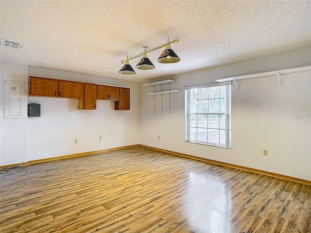 unfurnished room featuring a textured ceiling, light hardwood / wood-style floors, and electric panel