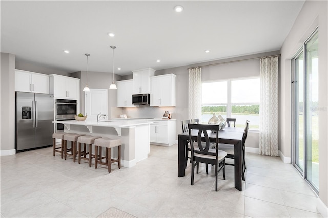 kitchen featuring tasteful backsplash, stainless steel appliances, a kitchen island with sink, decorative light fixtures, and white cabinets