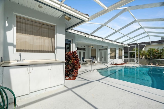 view of pool featuring glass enclosure, ceiling fan, a patio area, and sink