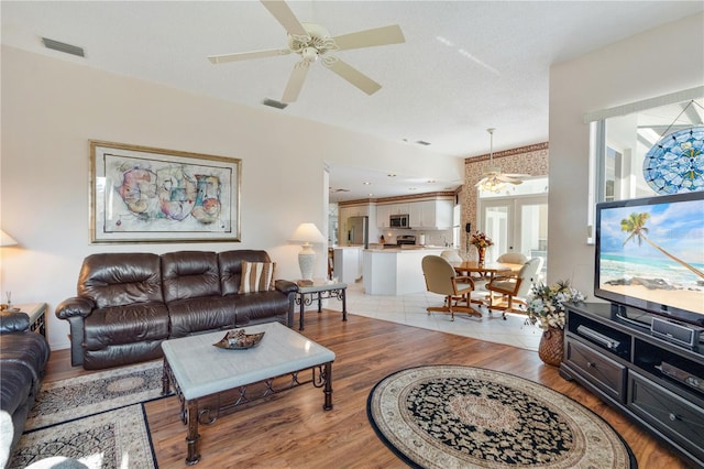 living room with ceiling fan, light hardwood / wood-style floors, and a textured ceiling