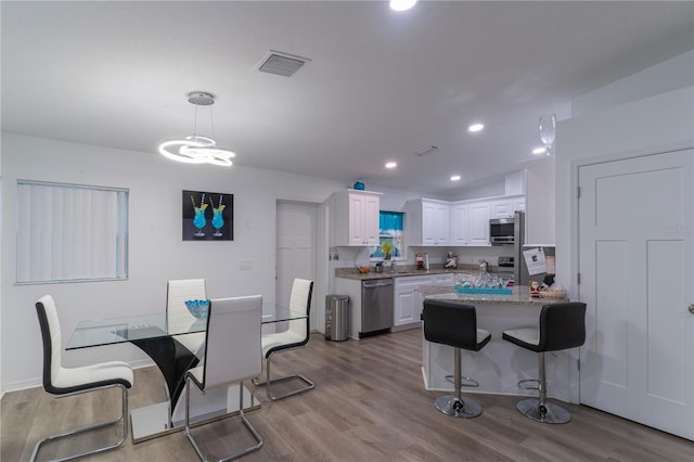 kitchen featuring light stone counters, stainless steel appliances, white cabinets, light hardwood / wood-style floors, and hanging light fixtures