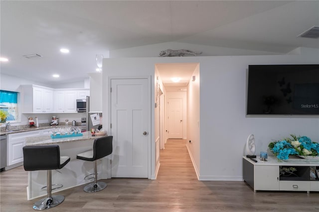 kitchen featuring appliances with stainless steel finishes, light hardwood / wood-style floors, light stone counters, white cabinetry, and a breakfast bar area