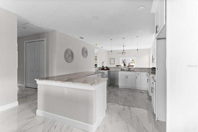 kitchen with kitchen peninsula, sink, decorative light fixtures, light stone counters, and white cabinetry