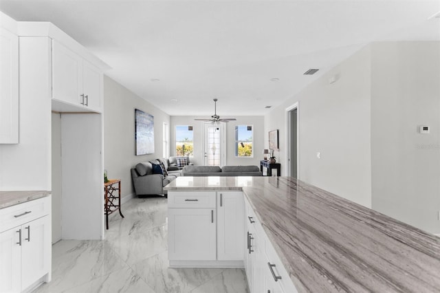 kitchen with white cabinetry, ceiling fan, and light stone countertops